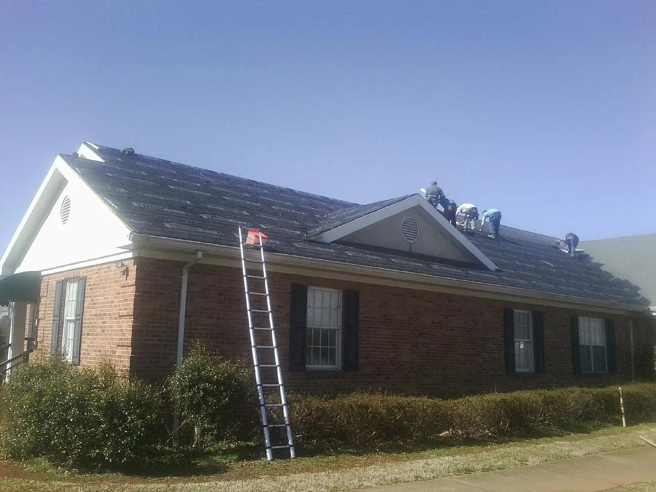 Crew tearing shingles off a brick ranch roof with a ladder set — Metal Roof Repair work by our crew in Plantersville