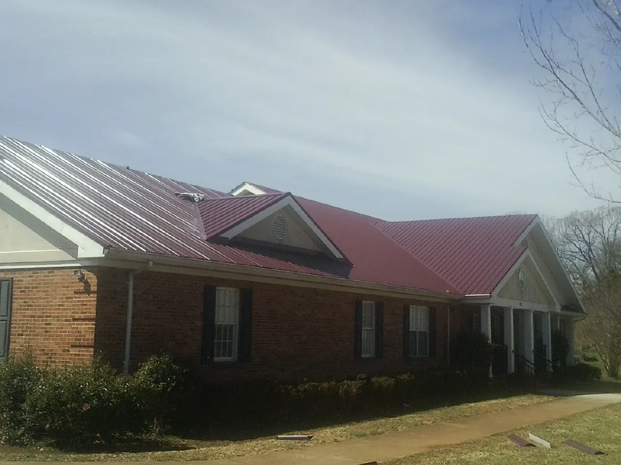 Red metal roof with gabled entries on a long brick building, from a Hail Damage Roof Repair job in Plantersville