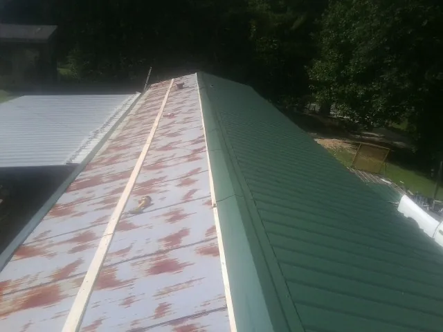 Old rusted panels beside newly installed green metal roofing in Plantersville