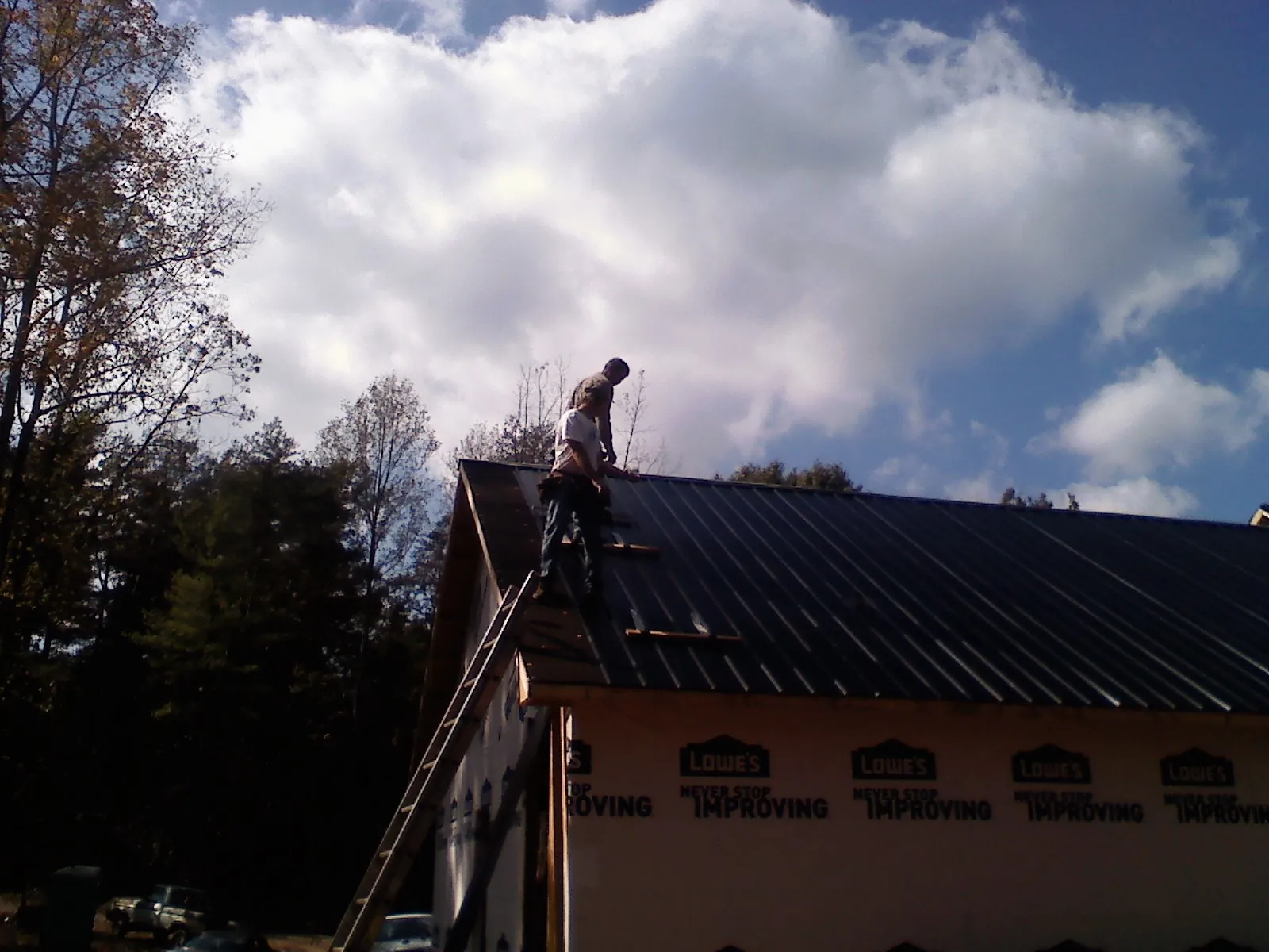 Roofer fastening dark metal panels high against a cloudy sky, from a Roof Inspection job in Plantersville